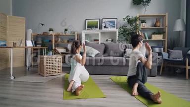 一对男女在公寓里练习瑜伽，坐在地板上扭动身体